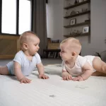 Gemelos gateando en una alfombra segura en casa